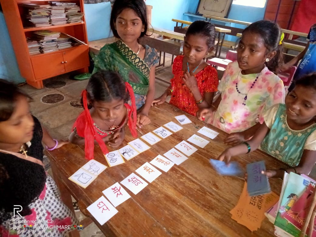 Children matching picture cards with Marathi words around a wooden table.