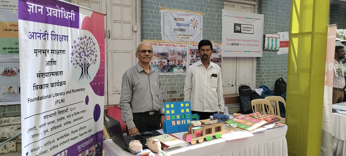 Anandi Shikshan stall with learning materials, puppets and a bilingual banner.